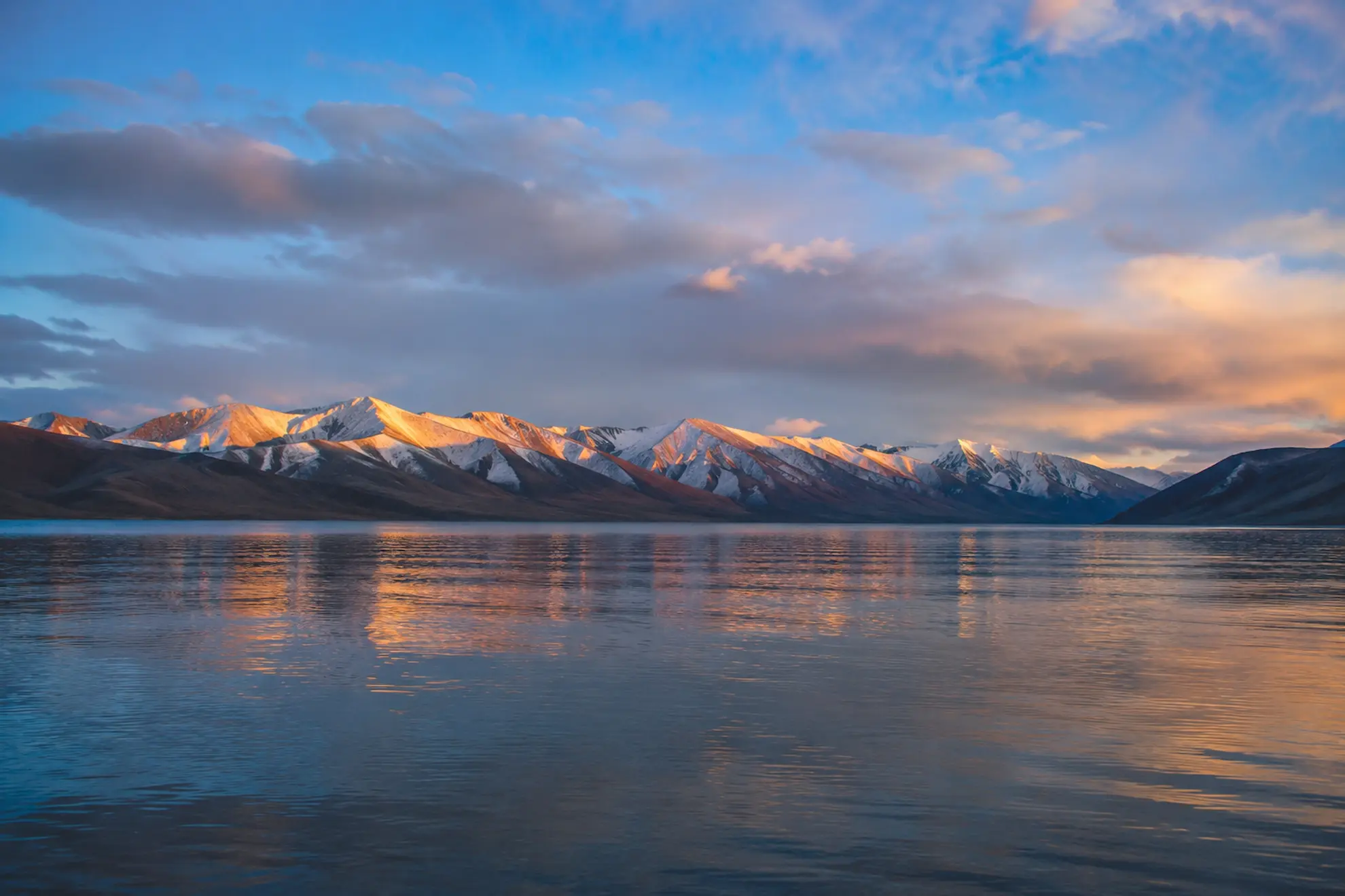 Golden sunrise light spreading across the surface of Pangong Lake in Ladakh